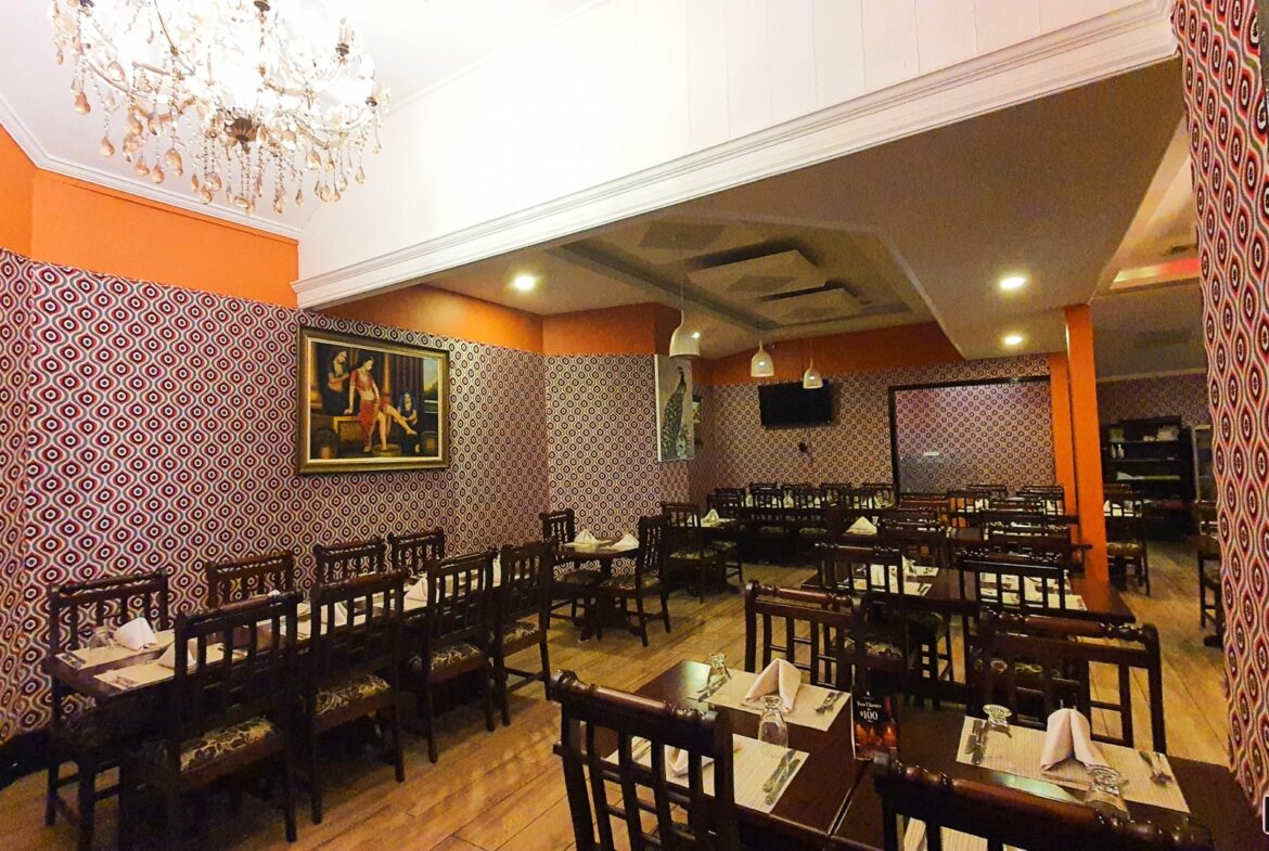 Elegant restaurant interior with patterned wallpaper, tables, chairs, and a chandelier.