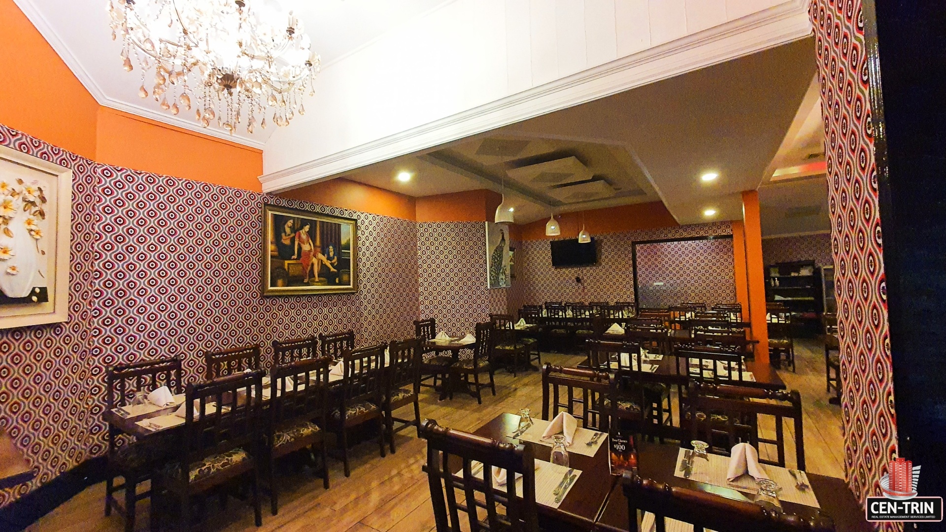 Elegant restaurant interior with patterned wallpaper, tables, chairs, and a chandelier.