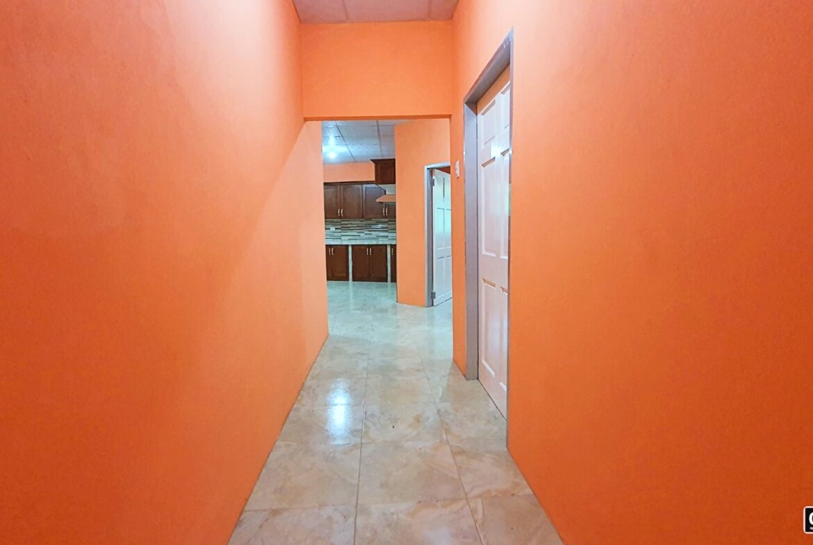 Empty hallway with orange walls leading to a kitchen