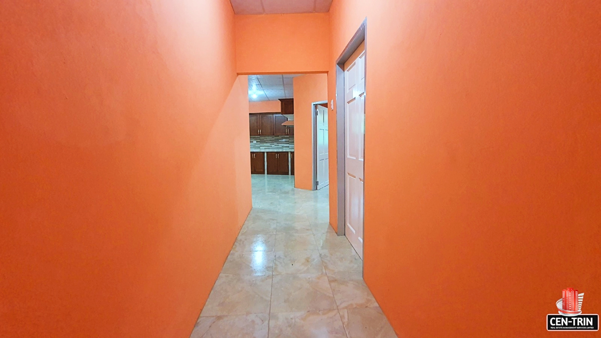 Empty hallway with orange walls leading to a kitchen