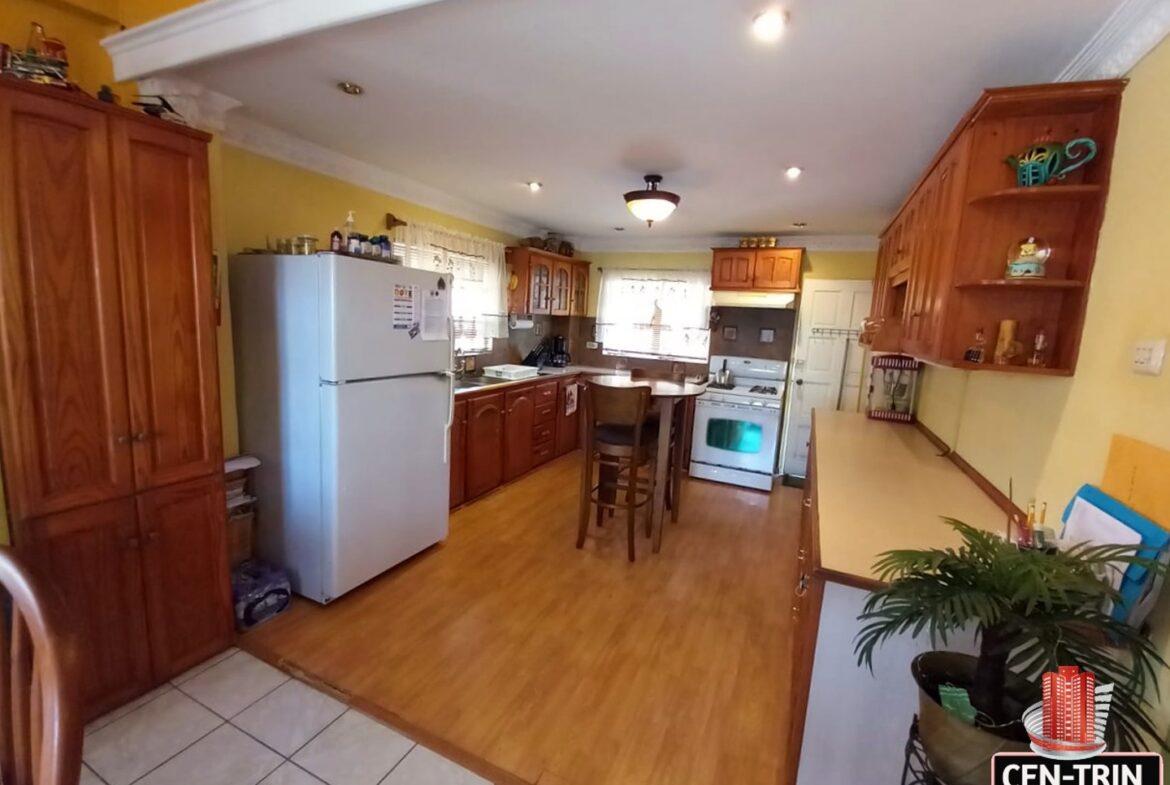 A kitchen with a refrigerator, stove, and table in a 3-bedroom house for sale.