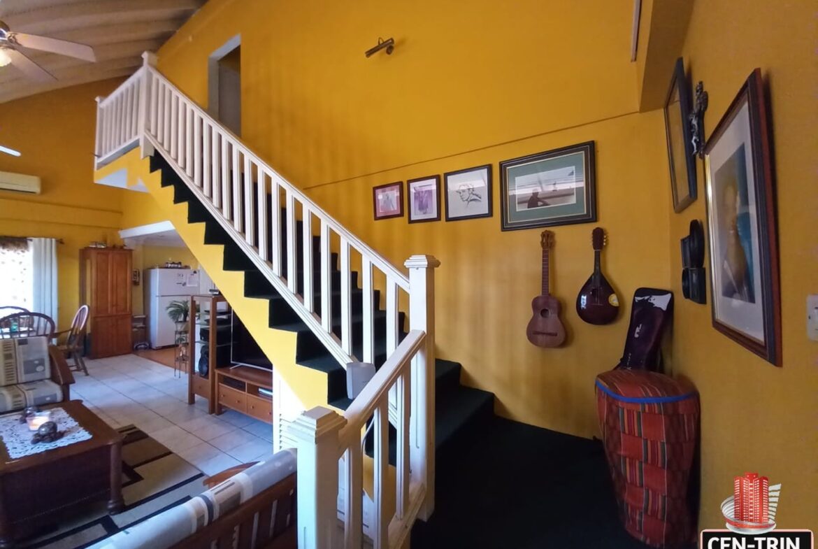 A living room with a staircase leading up to a second floor and two guitars hanging on the wall.