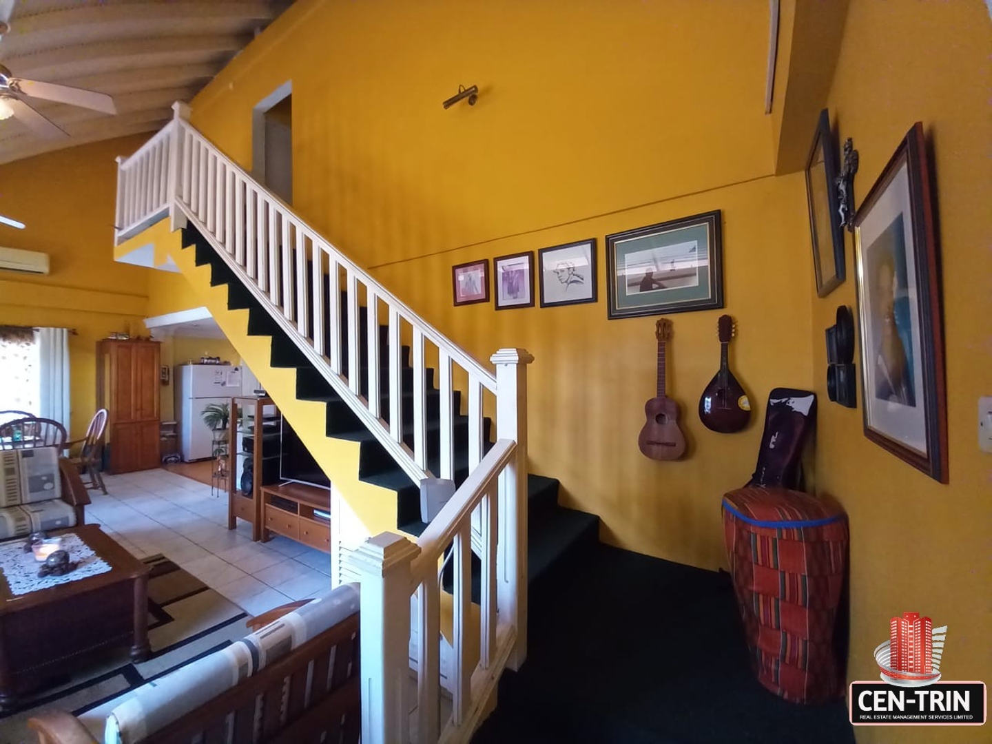 A living room with a staircase leading up to a second floor and two guitars hanging on the wall.