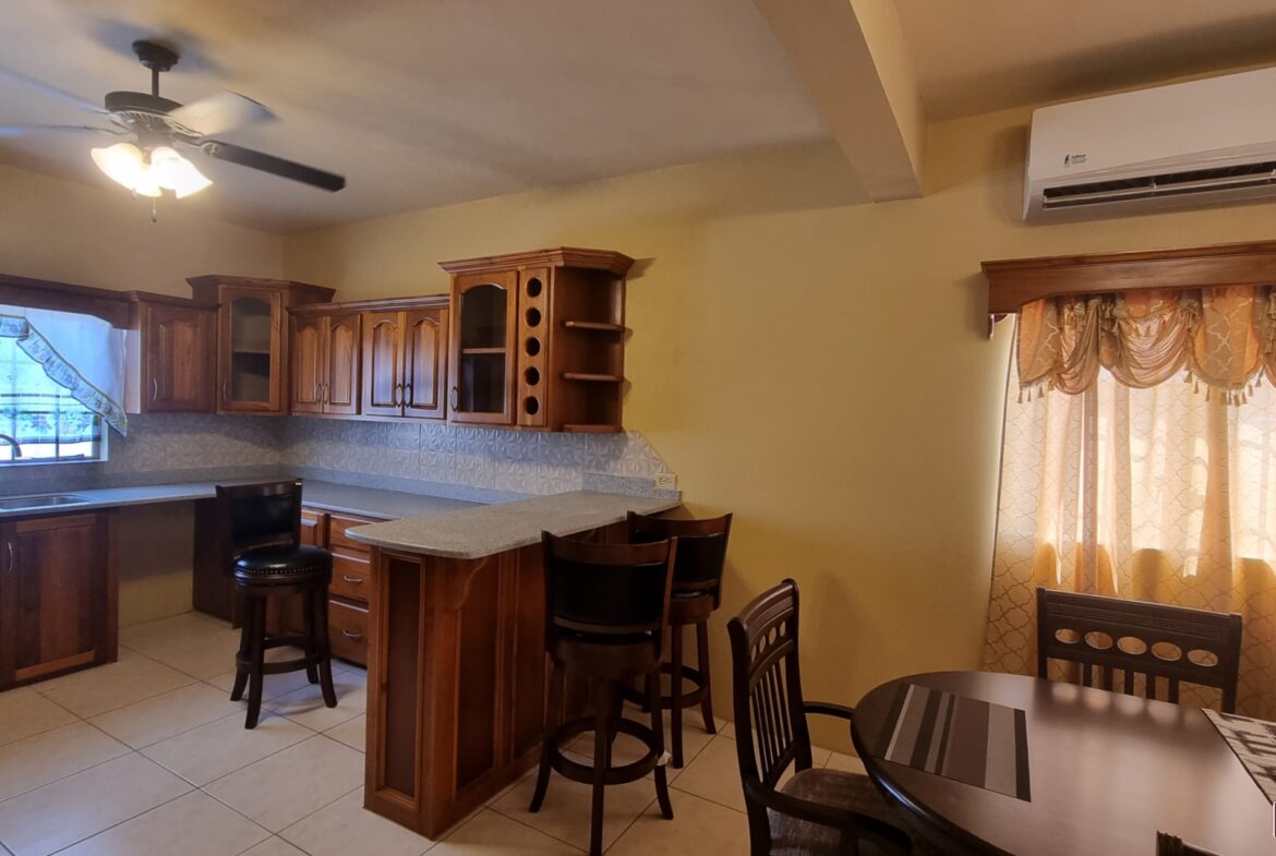 Kitchen area in townhouse for sale with wooden cabinets, sink, faucet, granite countertops, and stainless steel appliances. There is a window with a view of the backyard.