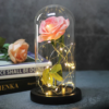 A preserved pink rose encased in a glass dome with warm LED lights, resting on a wooden base.