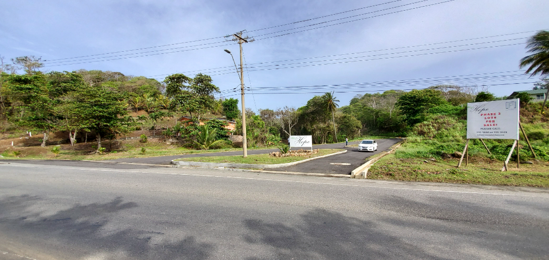 A close-up view of the entrance to Hope Estate, Tobago, with a prominent sign and lush greenery surrounding the gated community.