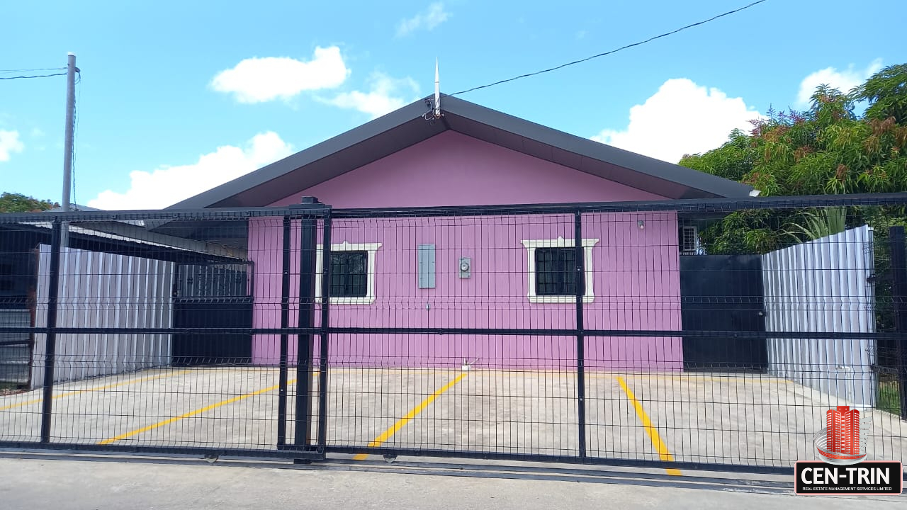 Front view of a pink one-story apartment building with a black metal security gate and a paved parking area of this lovely apartment for rent