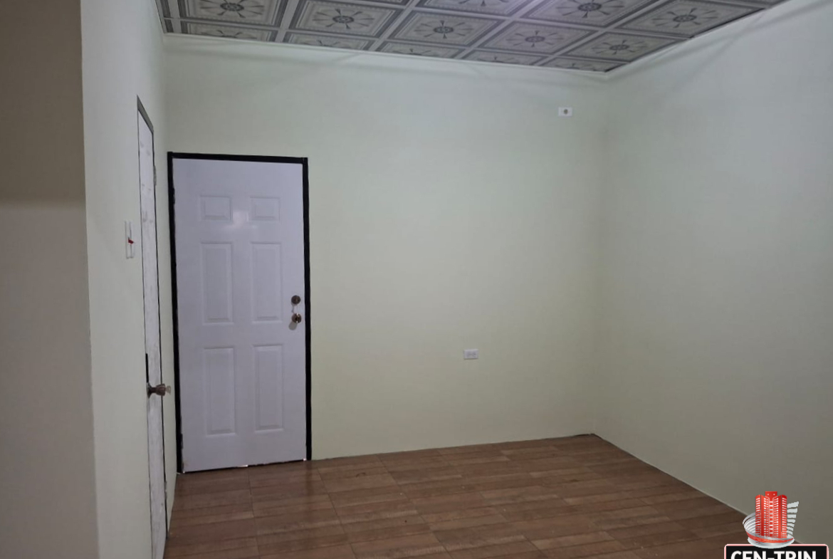 Interior view of an empty apartment room with light green walls, a decorative patterned ceiling, a white door with a black frame, and a tiled floor.