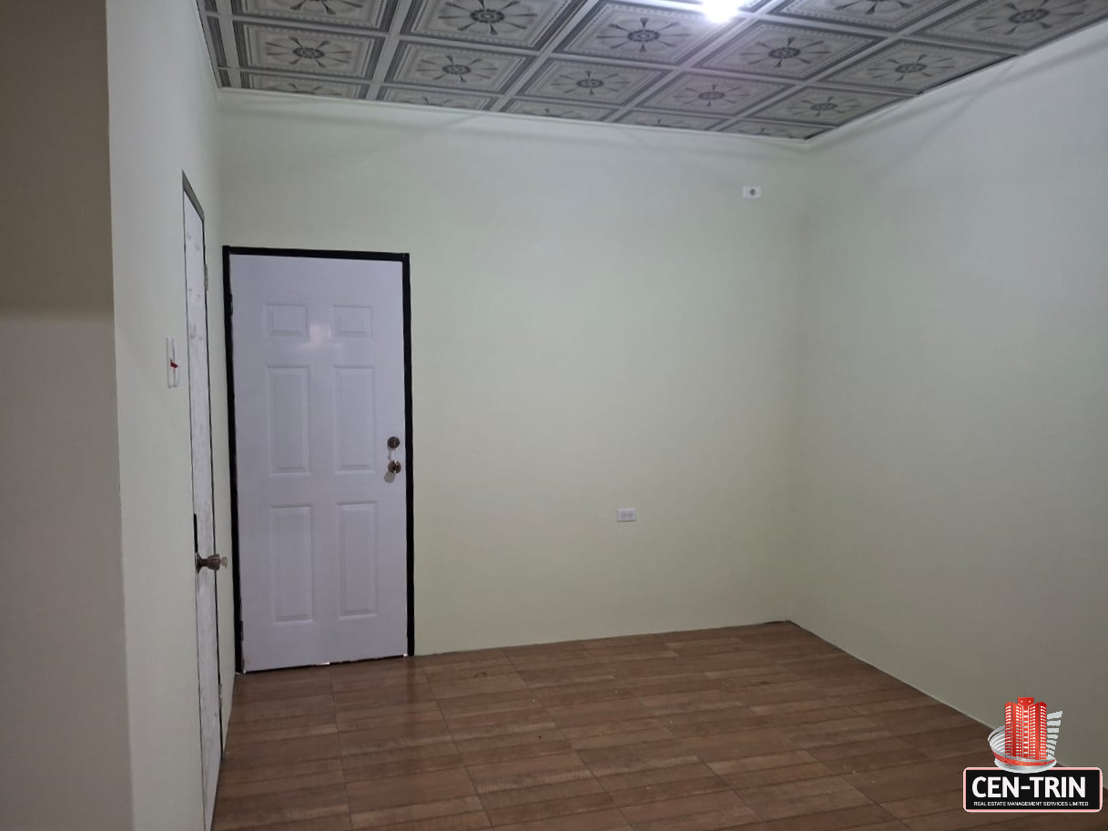 Interior view of an empty apartment room with light green walls, a decorative patterned ceiling, a white door with a black frame, and a tiled floor.