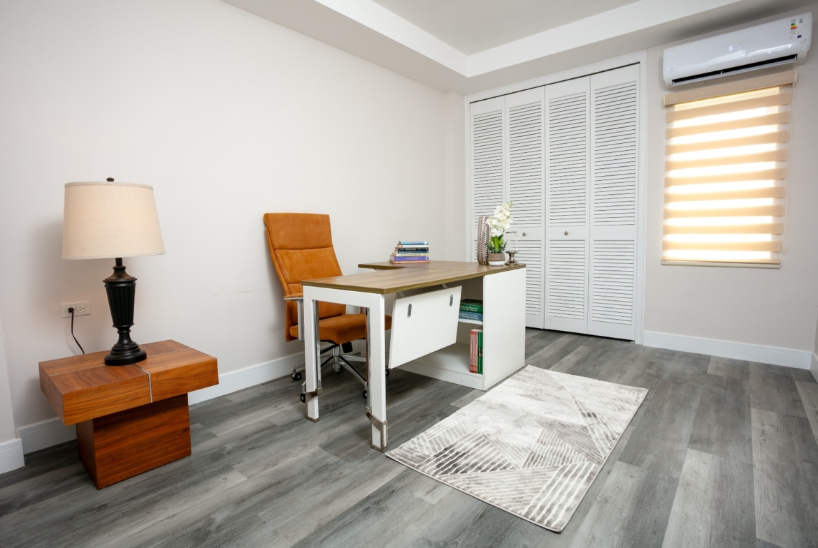 Home office at Roystonia Mews featuring a desk, chair, storage, air conditioning unit, and gray plank flooring.