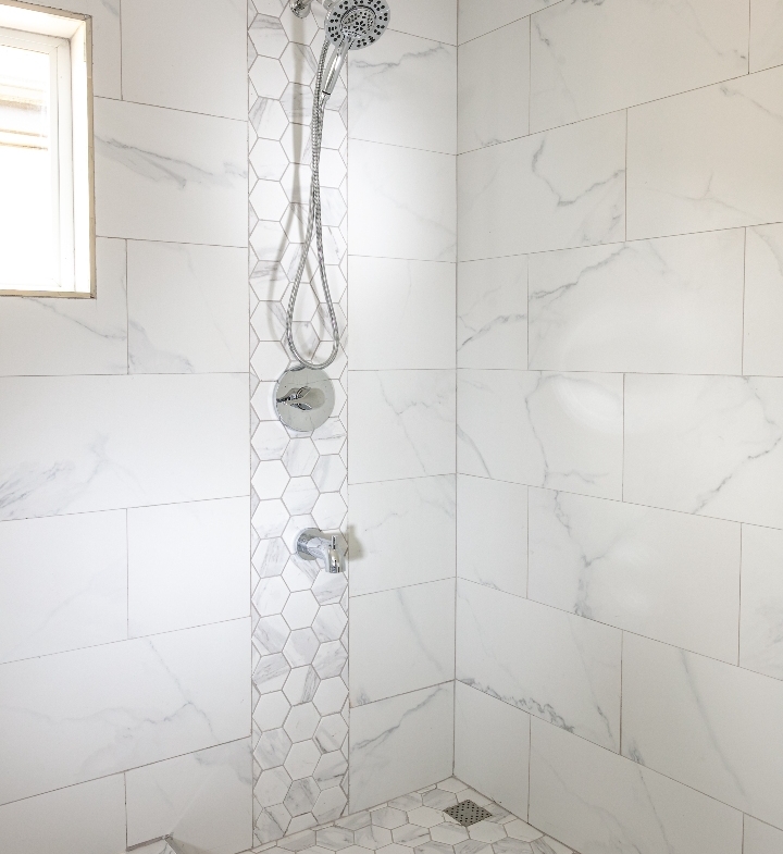 Modern shower at Roystonia Mews featuring Moen Engage Multi-Function Hand Shower and Magnetix Handheld Shower, white marble-like tile, and hexagonal tile accents.