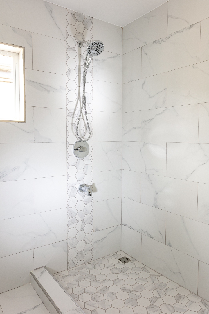 Modern shower at Roystonia Mews featuring Moen Engage Multi-Function Hand Shower and Magnetix Handheld Shower, white marble-like tile, and hexagonal tile accents.