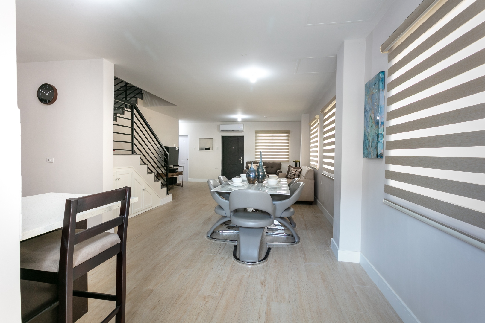 Wide interior view of Roystonia Mews, showing open concept living, dining area, staircase, and natural light from windows with blinds.