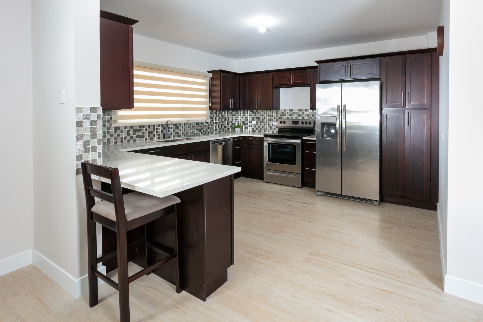 Modern kitchen at Roystonia Mews featuring dark wood cabinets, stainless steel appliances, a breakfast bar, and tiled backsplash.