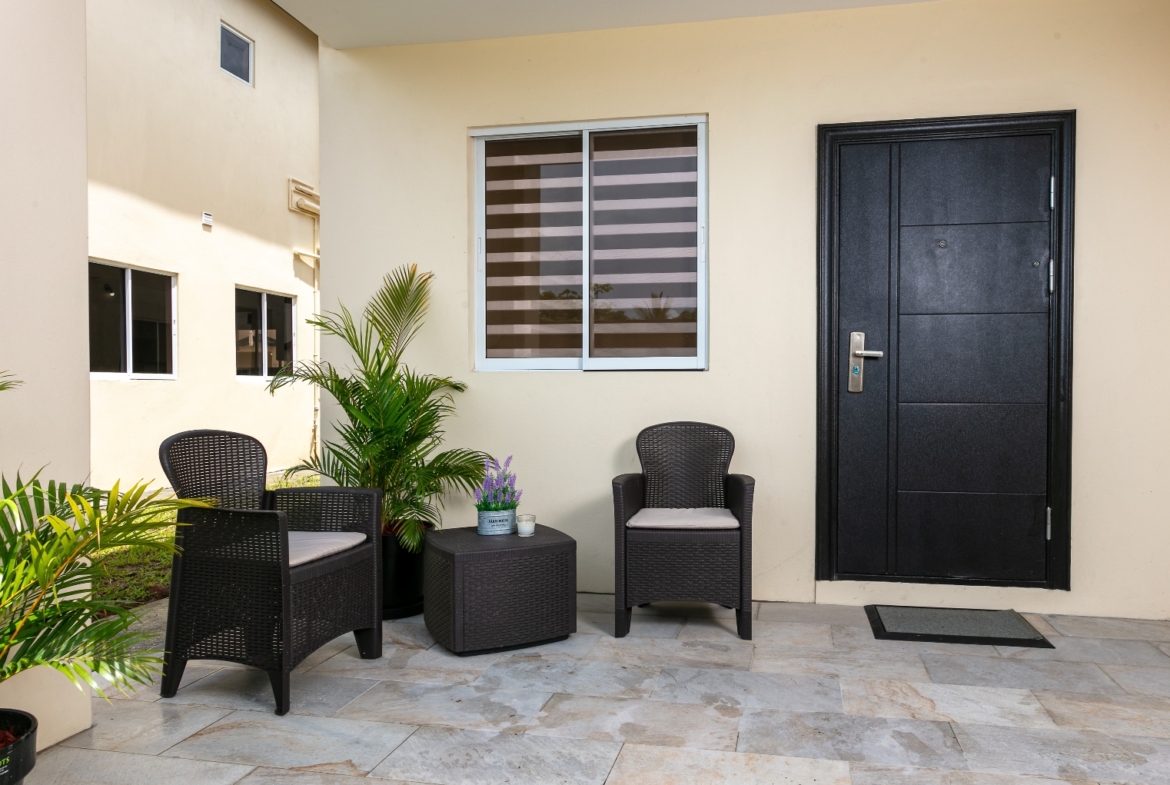 Outdoor patio entrance at Roystonia Mews featuring a dark front door, outdoor seating, potted plants, and tiled flooring.