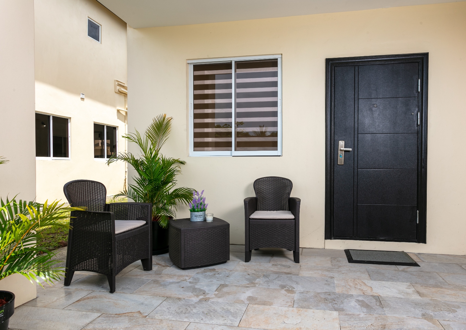 Outdoor patio entrance at Roystonia Mews featuring a dark front door, outdoor seating, potted plants, and tiled flooring.