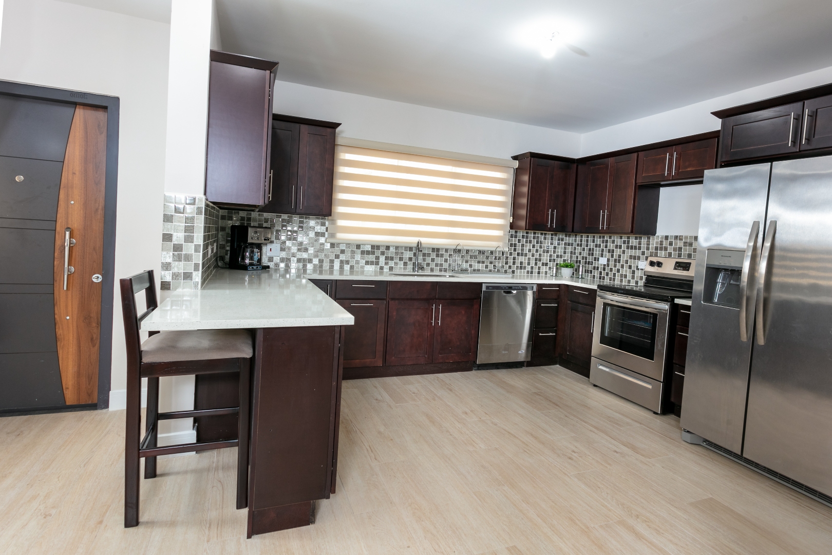 Kitchen at Roystonia Mews featuring dark wood cabinets, stainless steel appliances, a breakfast bar, tiled backsplash, and a unique doorway.